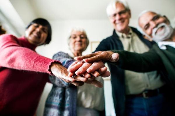 A group of older adults standing together with their hands stacked in the centre, showing unity and teamwork.