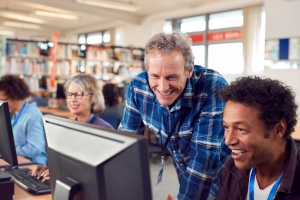 Photo of people using computers in a library with another person on hand to help with queries.