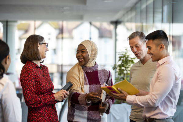 Group of adults standing holding digital tablets and devices, smiling and talking together
