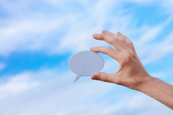 Image of hand holding a speech bubble with a blue sky background