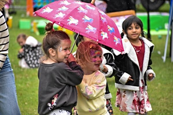 Two young girls with face paint smile while sheltering under an umbrella