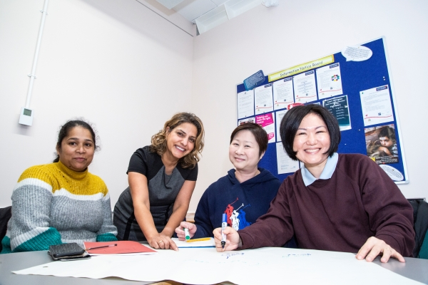 Group of 4 people in a class setting, smiling