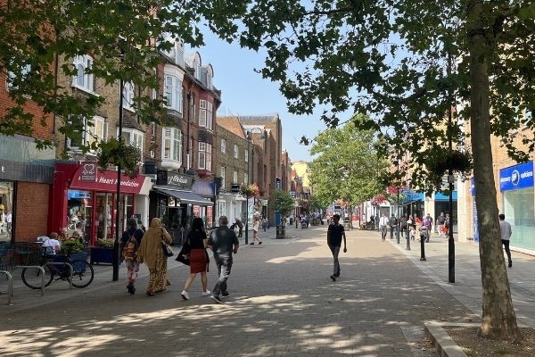 A photo of Uxbridge High Street featuring a mix of independent and chain stores, bicycles, and pedestrians.