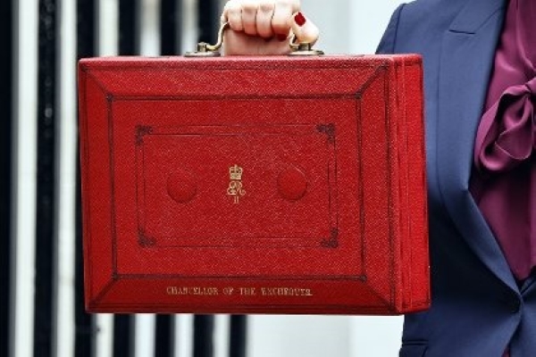 A photo of a red briefcase marked ‘Chancellor of the Exchequer,’ symbolizing government budget and funding decisions.