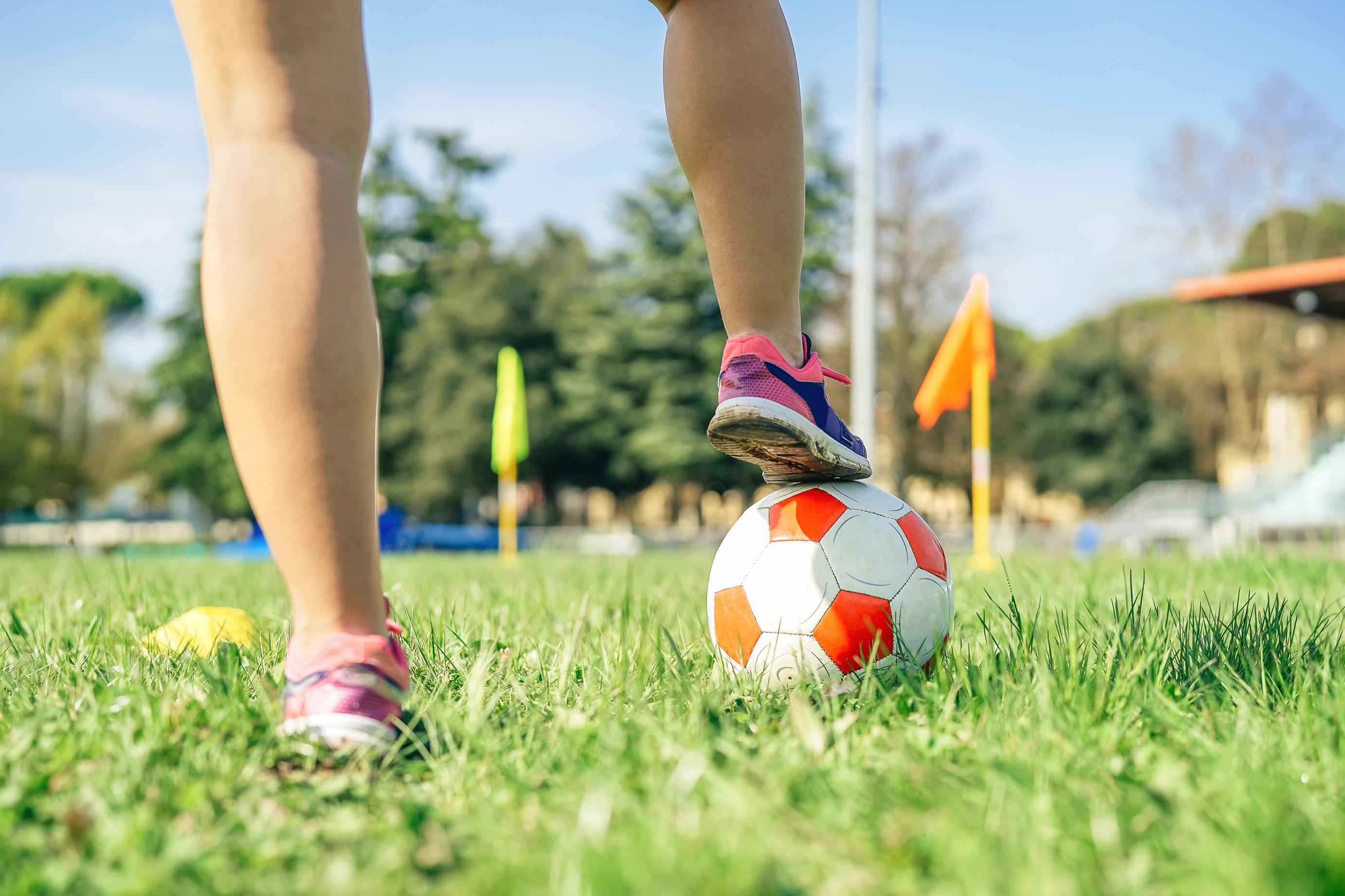 Foot placed on top of a football on grass in the park
