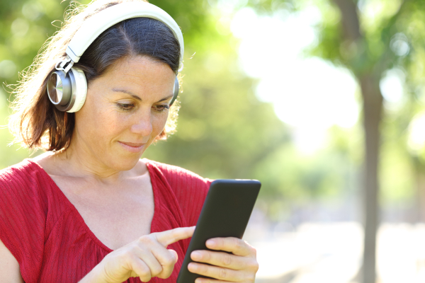 Photo of lady outside, wearing headphones, listening to an audio on her mobile phone