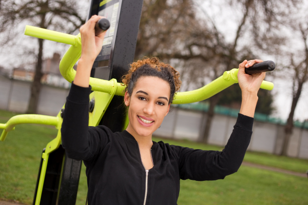 Young woman using the outdoor gym equipment in the park, smiling