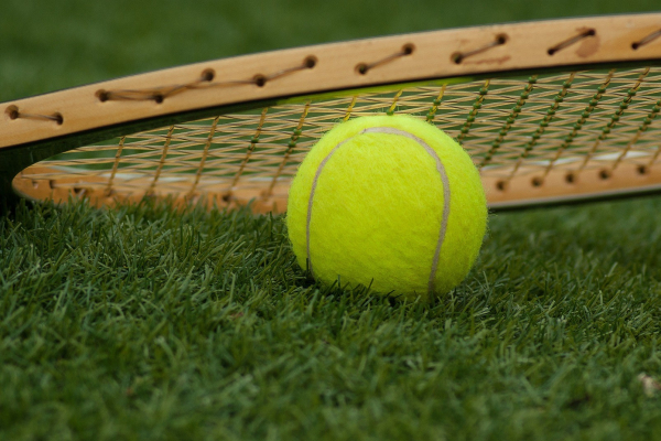 Close up photo of tennis ball and racquet on grass.